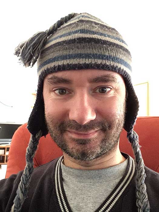 Cédric Trévisan wearing a mostly gray (but with a couple blue stripes) knit hat with ear flaps.