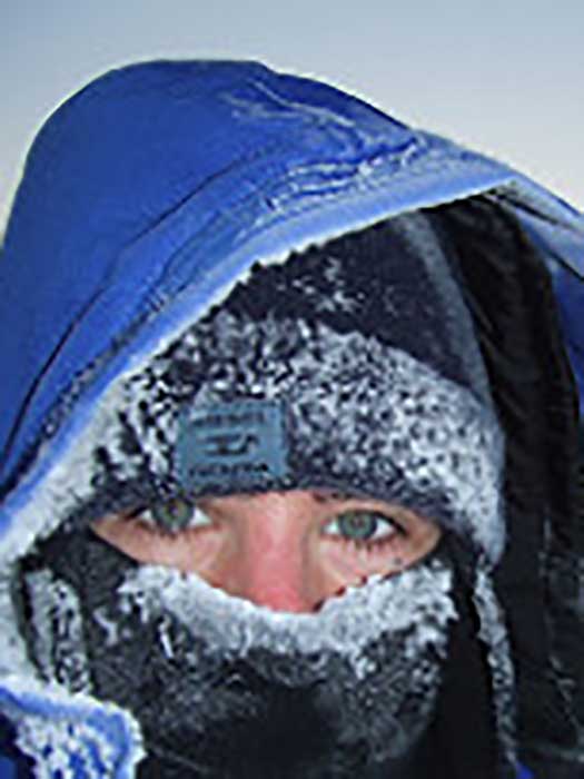 Henny Swan wearing a blue beanie, blue face mask, blue anorak hood, all covered in ice, somewhere in the arctic.