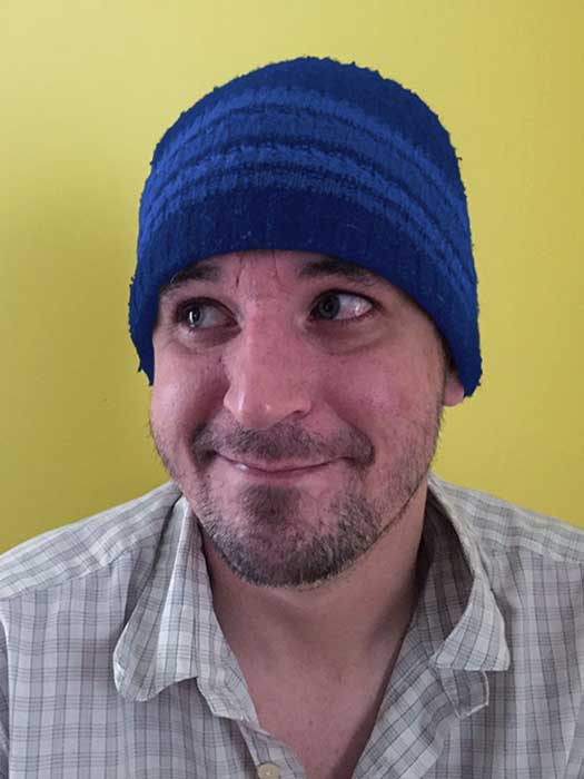 Jon Metz with a striped blue beanie and an expression that, well, I really have no idea why they let me write this alt text because I have no idea what he is doing.