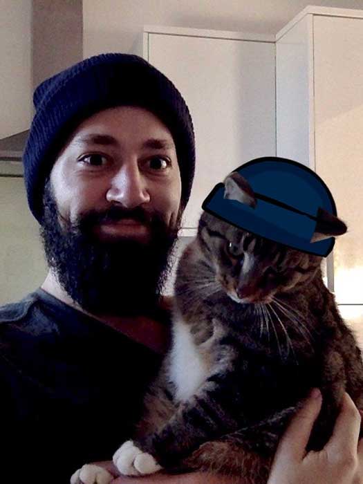 Michiel Bijl and his cat each wearing a blue beanie (that cat’s is a cartoon hat).