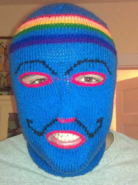 Shane Paciello wearing a knit blue full-face mask with eyebrows a mustache, some rainbow stripes, and red edges around the eyes and mouth.