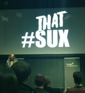 Billy Gregory presenting at Funka conference, with a huge "That #SUX" behind him.