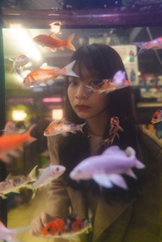 Maria of Santa Barbara, California standing behind a clear fish tank filled with goldfish.