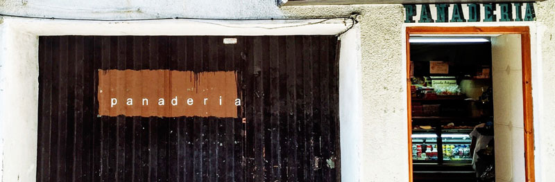 Street view of panaderia (bread shop) in Spain, with a closed garage type door and an open shop door