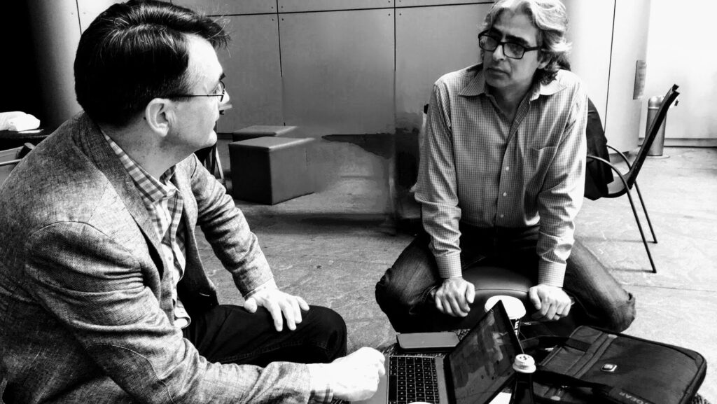 black and white photo of Charlie Pike (left) and Dave O'Neill chatting over a coffee in a forecourt of a New York coffee shop.