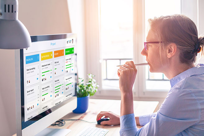 a person sitting at their desk using a mouse to interact with their desktop computer reviewing an agile KanBan board.