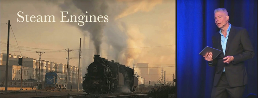Mark Pesce stands next to a slide showing an old fashioned steam train, with the title Steam Engines.